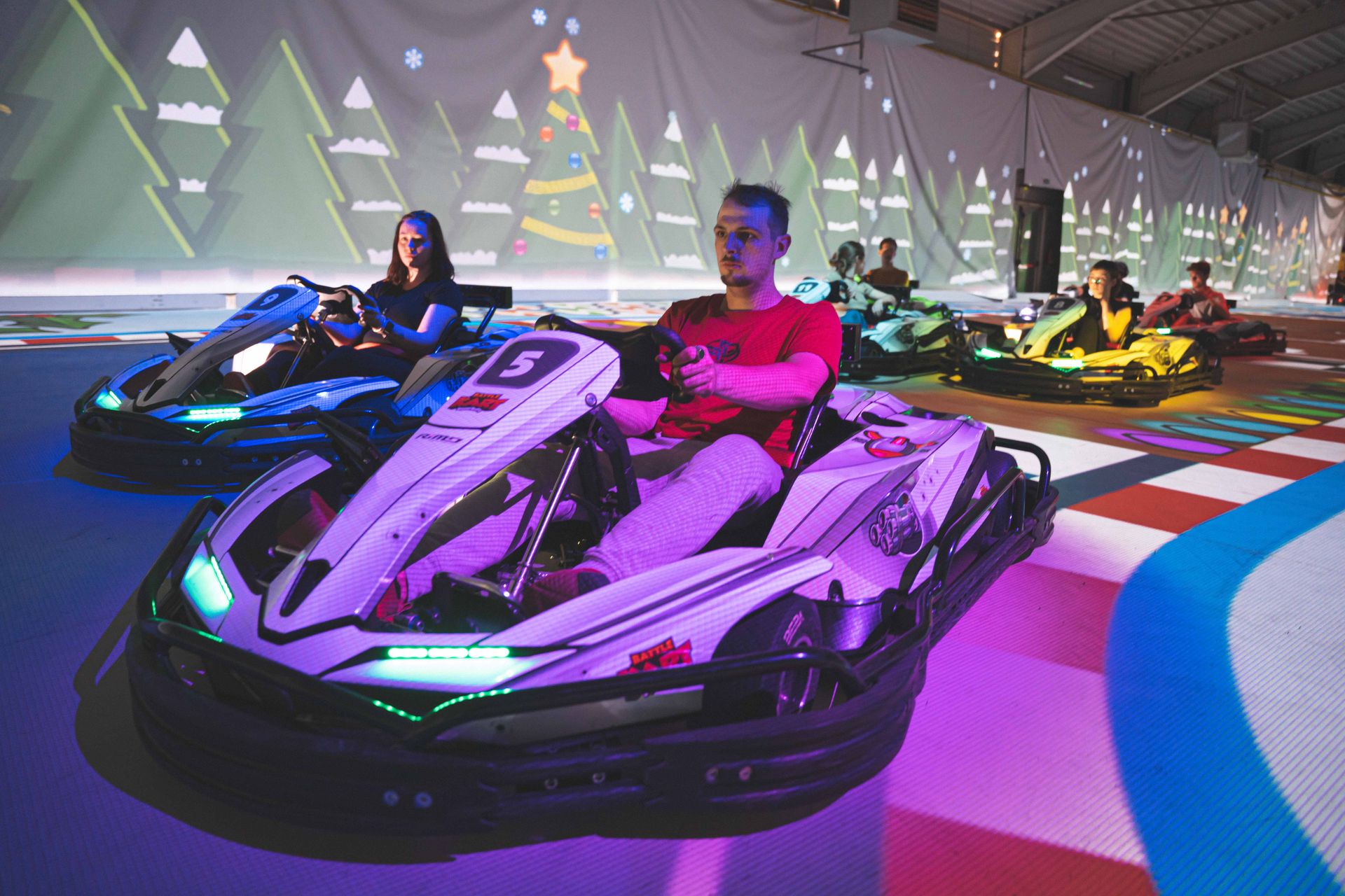 Een actievolle close-up van een elektrische kart op een verlichte indoorbaan. De belichting is modern met blauwe en paarse accenten.